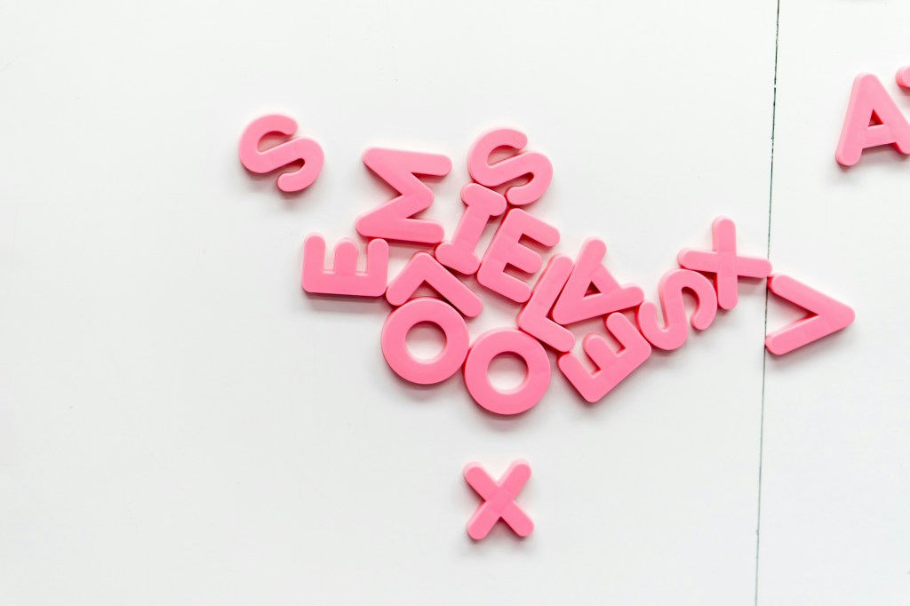 Pink magnets shaped like letters of the alphabet are randomly placed on a white background.